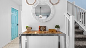 Un couloir avec une console en bois, un miroir orné d’oreilles d’ours, une porte bleue et un escalier.