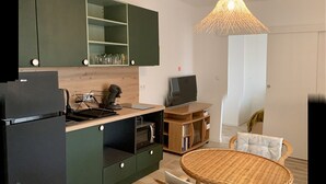 Een compacte keuken met donkergroene kastjes, een ingebouwde magnetron en een eethoek met een rieten tafel en stoelen.