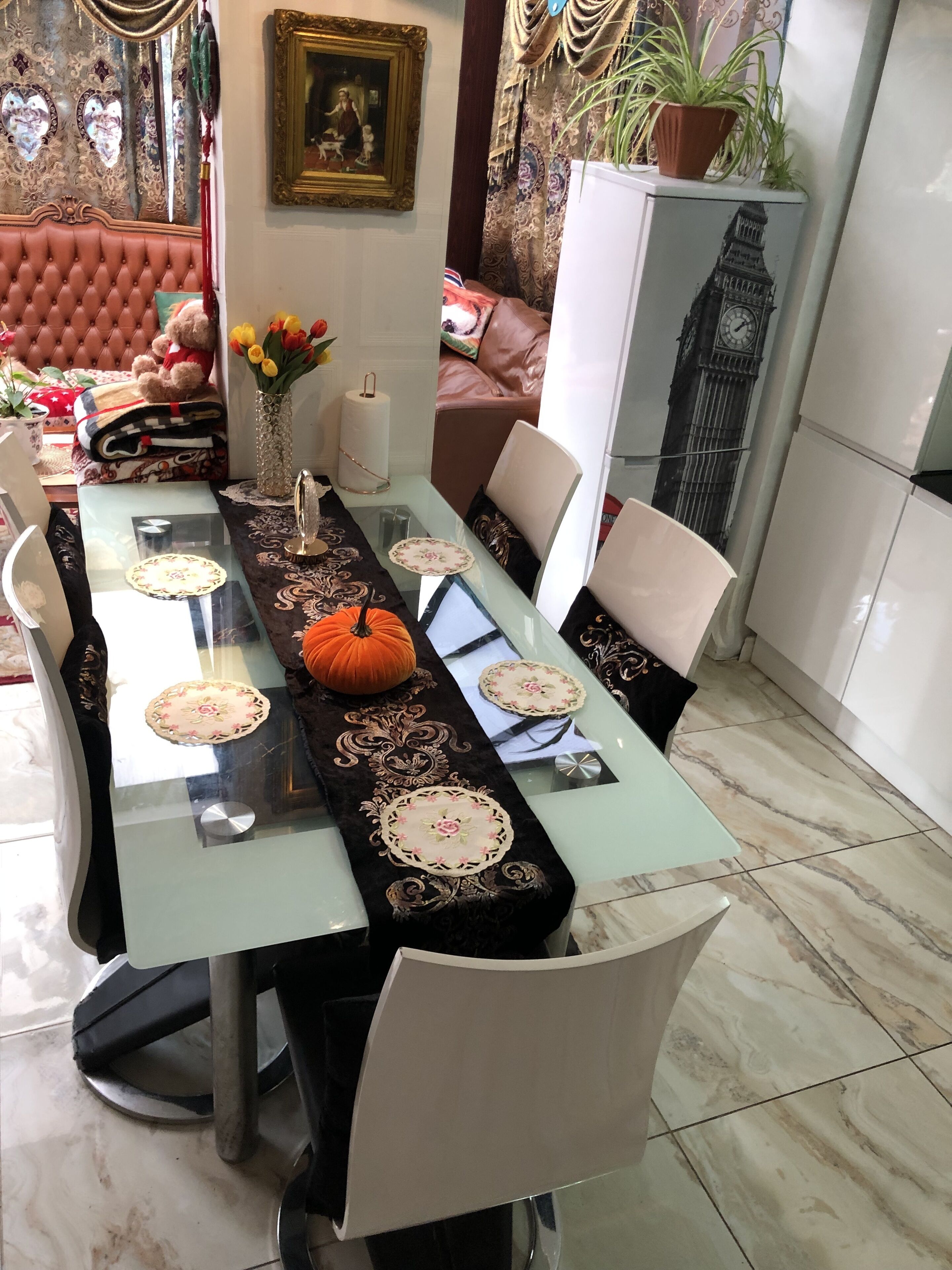 A dining area with a glass-top table, black table runner with floral patterns, and a pumpkin centerpiece.