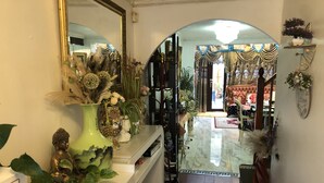 A hallway with a Buddha statue, a green vase with dried flowers, and a mirror on the left.
