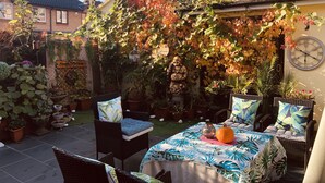 A patio with wicker furniture, a table with a tropical print tablecloth, and a clock on the wall.
