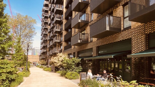 A modern urban street with a café on the right, featuring outdoor seating and a brick facade.