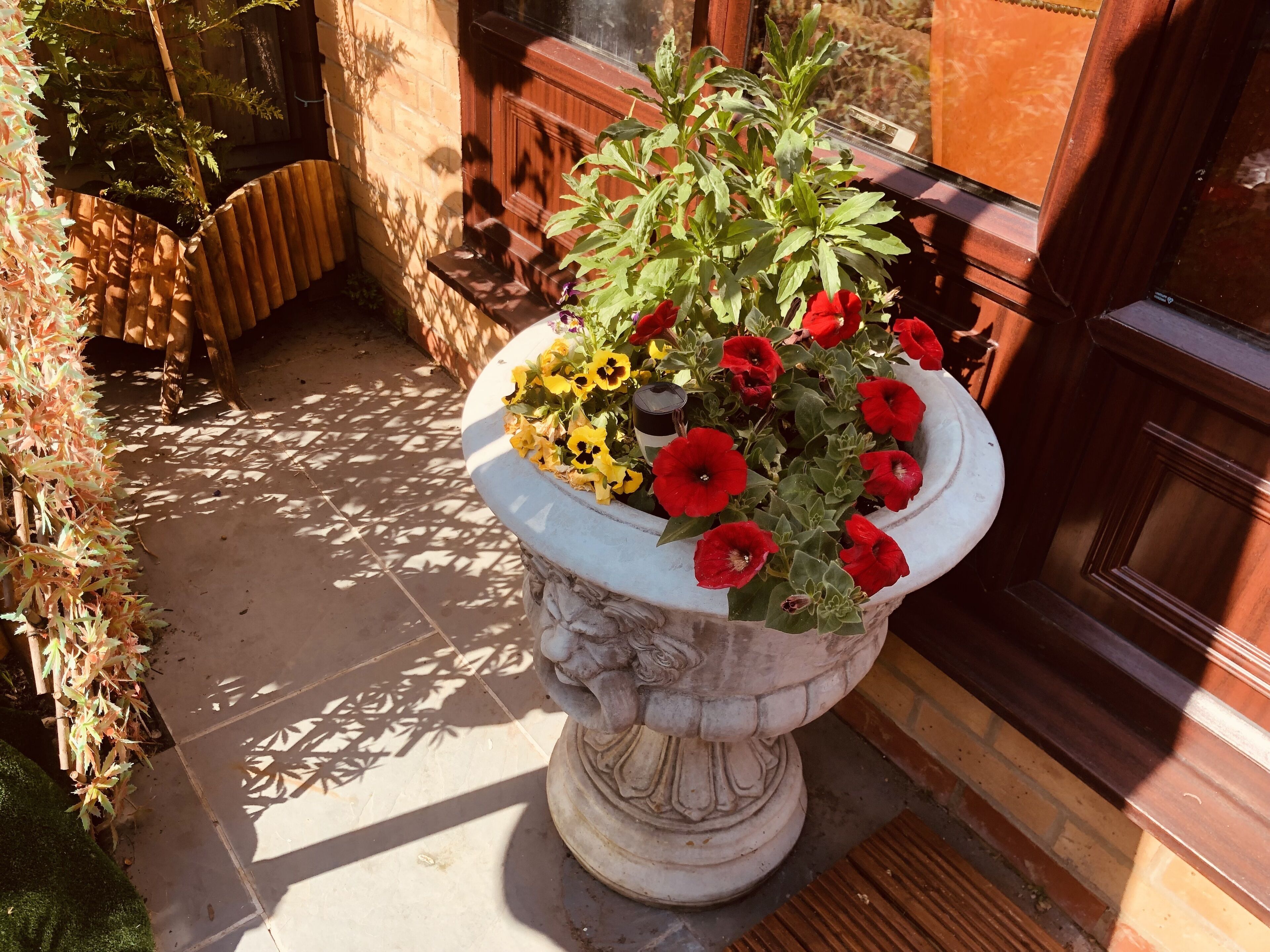 Una jardinera de piedra con flores rojas y amarillas, ubicada en un patio empedrado.