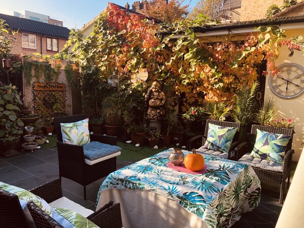 A cozy outdoor seating area with wicker furniture, a table with a tropical leaf tablecloth, and a decorative pumpkin centerpiece. - Centrally Located 4 Bedroom House  (London)