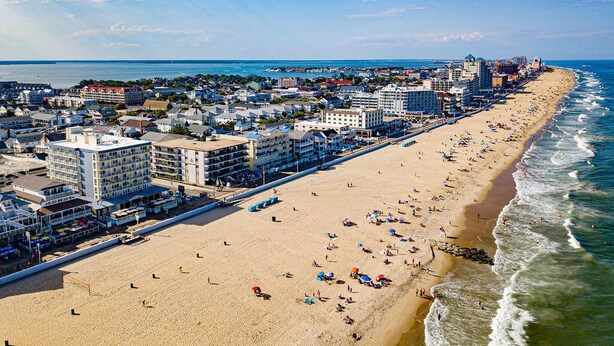 En kystby med en lang sandstrand, hoteller ved stranden og en klar blå himmel.