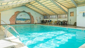 Indendørs swimmingpool med et muralmaleri af en strand, liggestole og et overdækket tag.