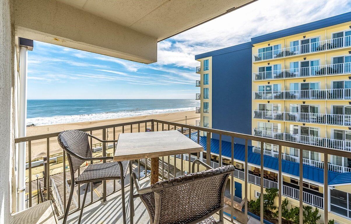 Ein Balkon mit Korbmöbeln, der auf einen Strand und ein mehrstöckiges Gebäude blickt.