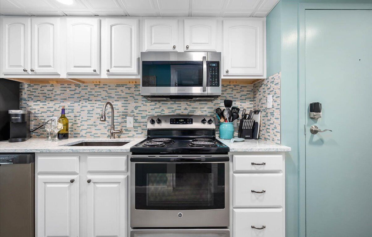 A kitchen with white cabinets, a stainless steel microwave, a stove, and a tiled backsplash.