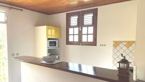 Eine Küche mit Holzboden, einer Mikrowelle, einem gelben Schrank, einem Fenster mit Jalousien und einer gefliesten Spritzschutzwand.
