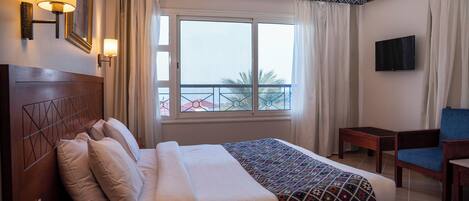 A hotel room with a bed, a bedside telephone, a television, and a view of the outside.
