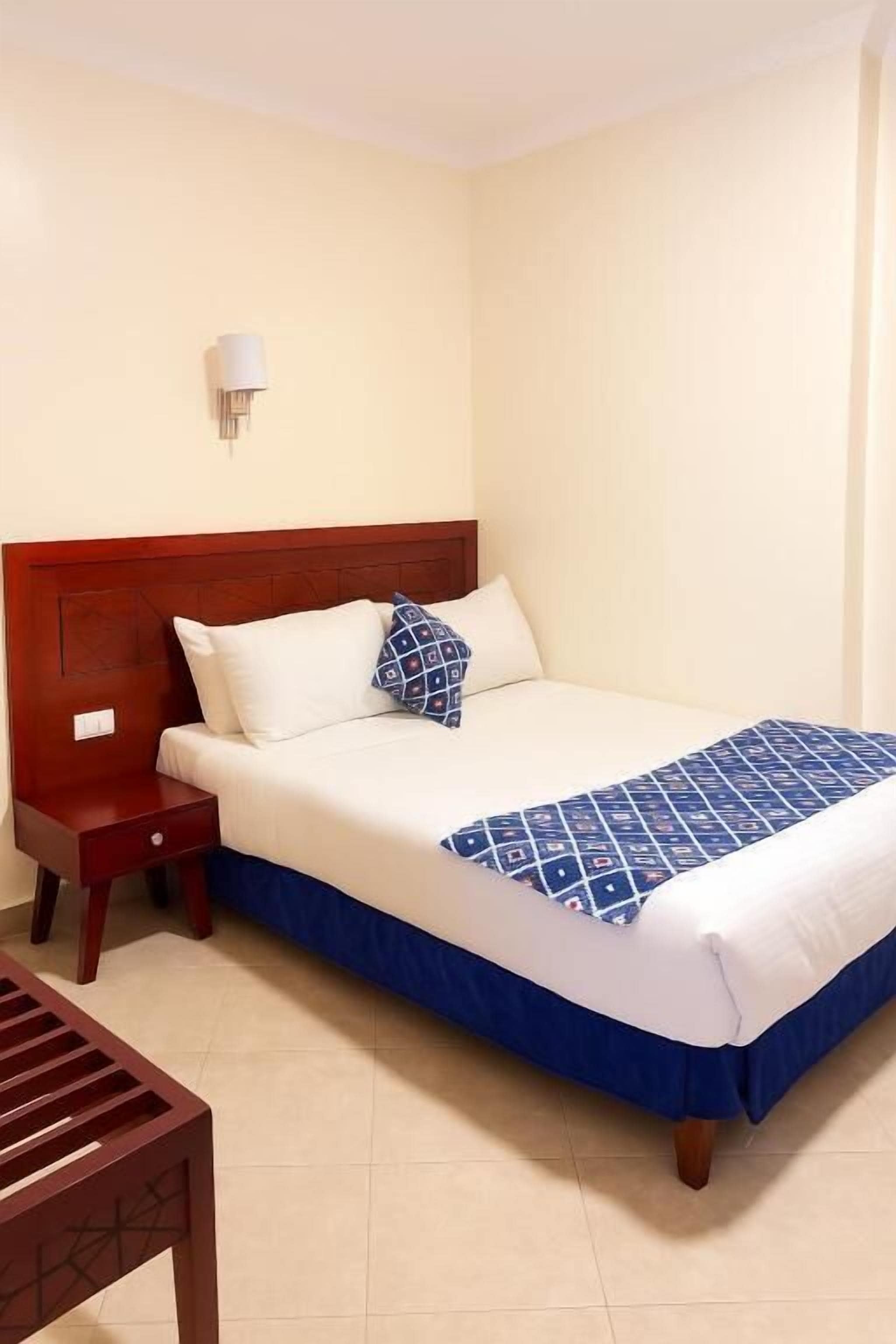 A neatly made bed with a blue and white bedspread, a wooden nightstand with a lamp, and a wooden chair.