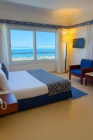 Camera d'albergo con un letto, una sedia, una scrivania, una TV e vista sull'oceano.