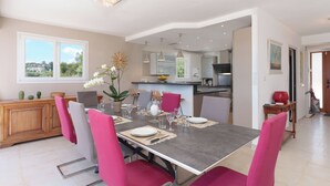 Un comedor con una mesa preparada para cuatro personas, rodeada de sillas, y una cocina al fondo.