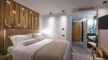 A modern hotel room with a large bed, a wooden headboard, a bedside table with a phone, and a bathroom with a mirror and sink.