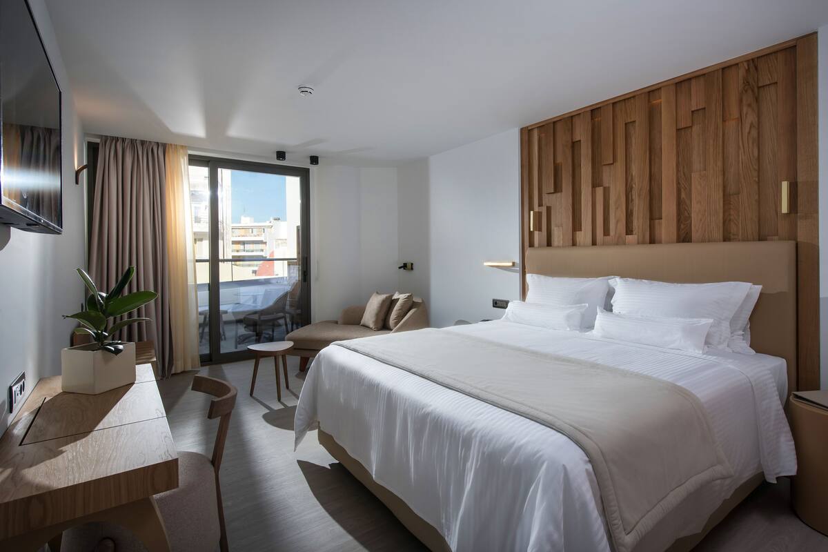 Een moderne hotelkamer met een groot bed, een bureau, een stoel en een balkon met uitzicht op de stad.