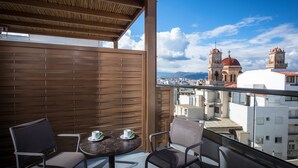 Een balkon met twee stoelen en een tafel, met uitzicht op een stadsgezicht met twee opvallende klokkentorens.