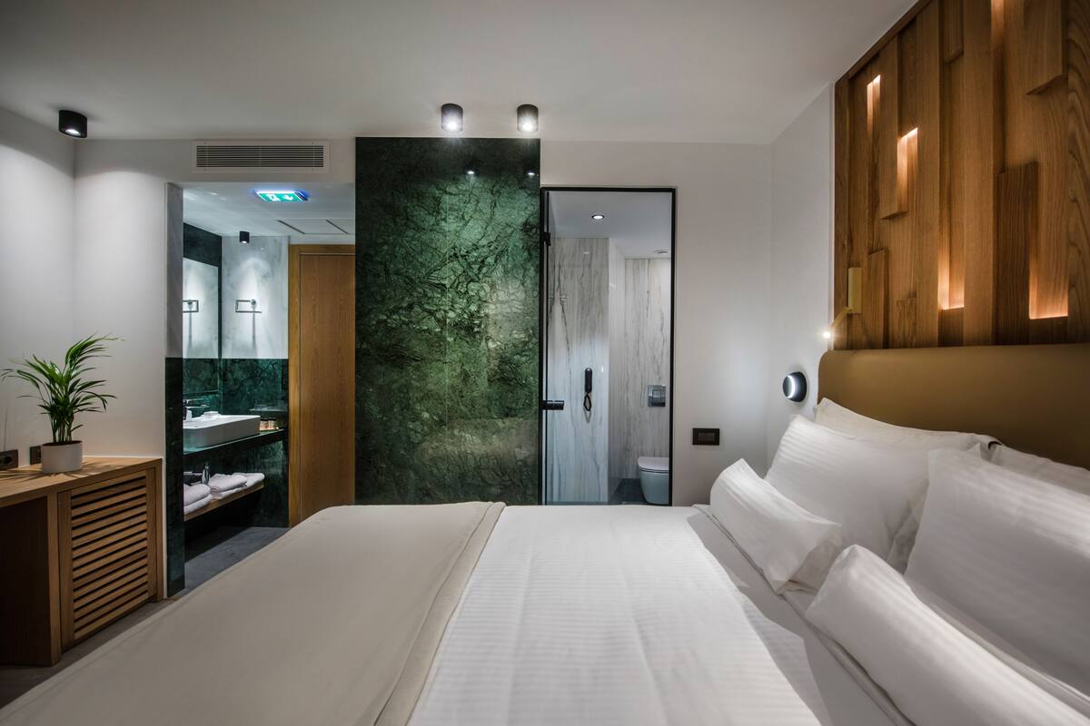 Een moderne hotelkamer met een groot bed, een houten hoofdeinde, een marmeren wand, een ingebouwd wastafelmeubel en een douchecel.