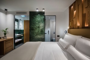 Una habitación de hotel moderna con una cama grande, cabecera de madera, pared de mármol, lavamanos integrado y zona de ducha.