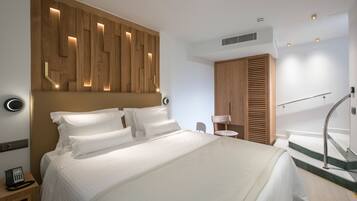 Ein modernes Hotelzimmer mit einem großen Bett, einem Holzkopfteil mit integrierter Beleuchtung, einem kleinen Nachttisch mit Telefon und einer Treppe mit Handlauf.