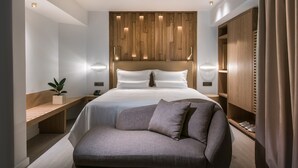 Een moderne slaapkamer met een groot bed, een houten hoofdbord, nachtkastjes, een bankje en een garderobe.