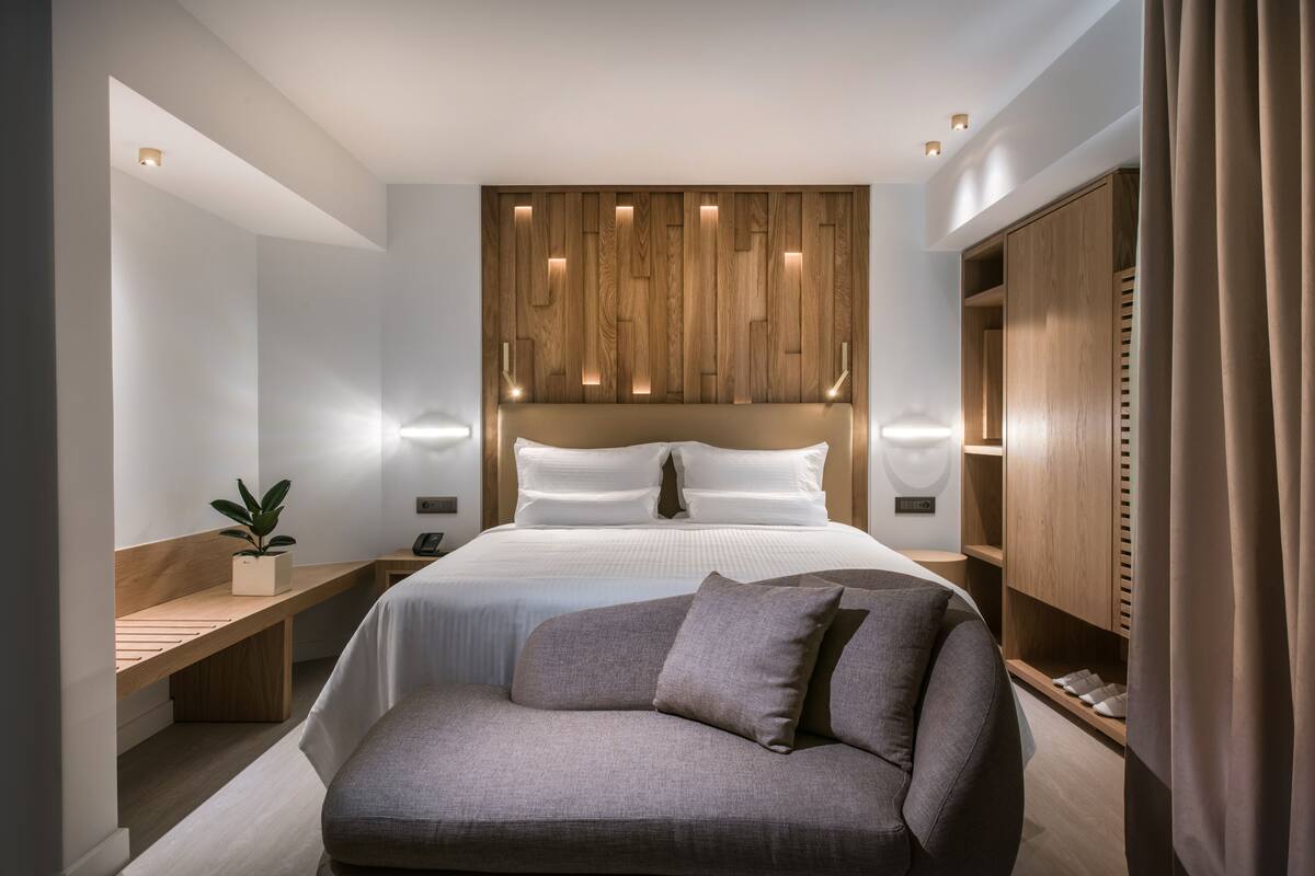 Een moderne slaapkamer met een groot bed, een houten hoofdbord, nachtkastjes, een bankje en een garderobe.
