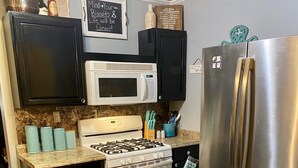Une cuisine compacte équipée d’un réfrigérateur en acier inoxydable, d’un four à micro-ondes blanc, d’une cuisinière et d’un lave-vaisselle. On y trouve également des objets décoratifs sur le plan de travail et un tableau noir sur lequel est inscrite une citation inspirante.