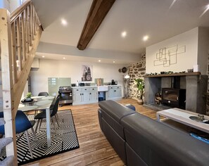 Een moderne woonkamer met een open haard, een eethoek en een keuken op de achtergrond, met een trap naar een hoger niveau.