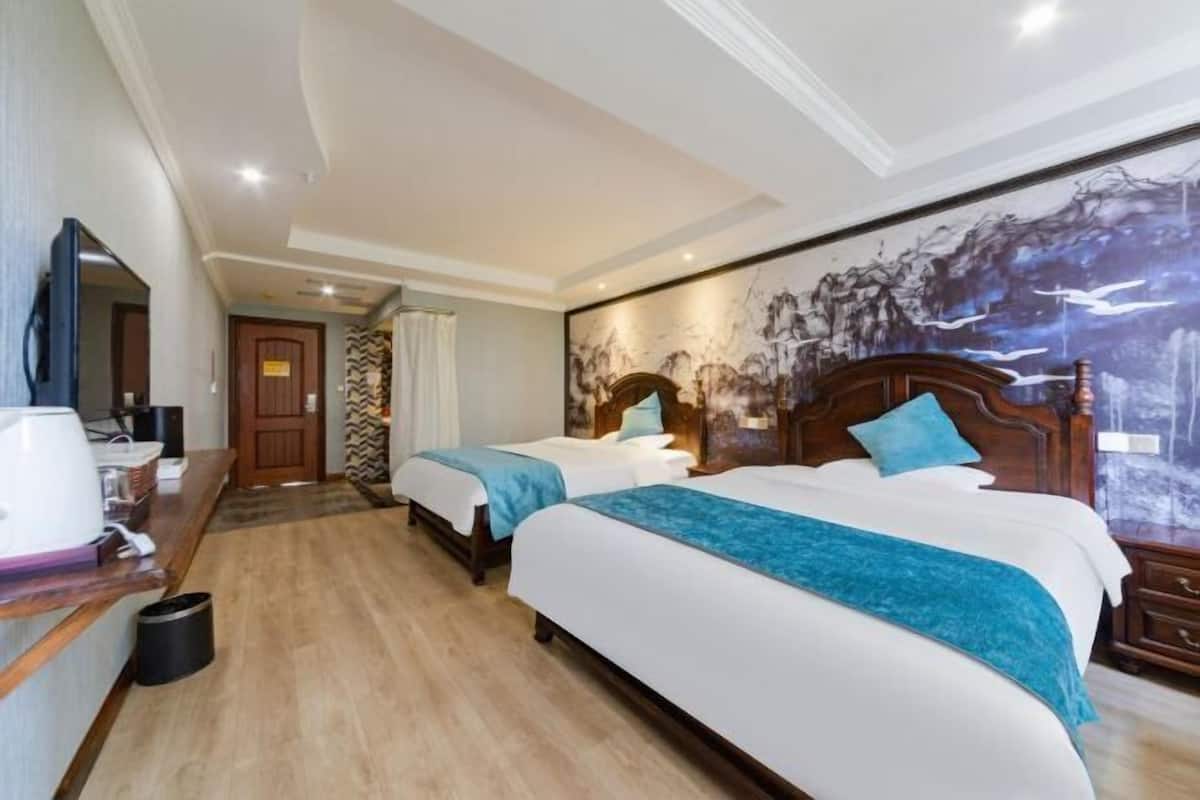 Ein Hotelzimmer mit zwei Betten, einem großen Gemälde an der Wand, Holzboden und einem Schreibtisch mit Lampe.