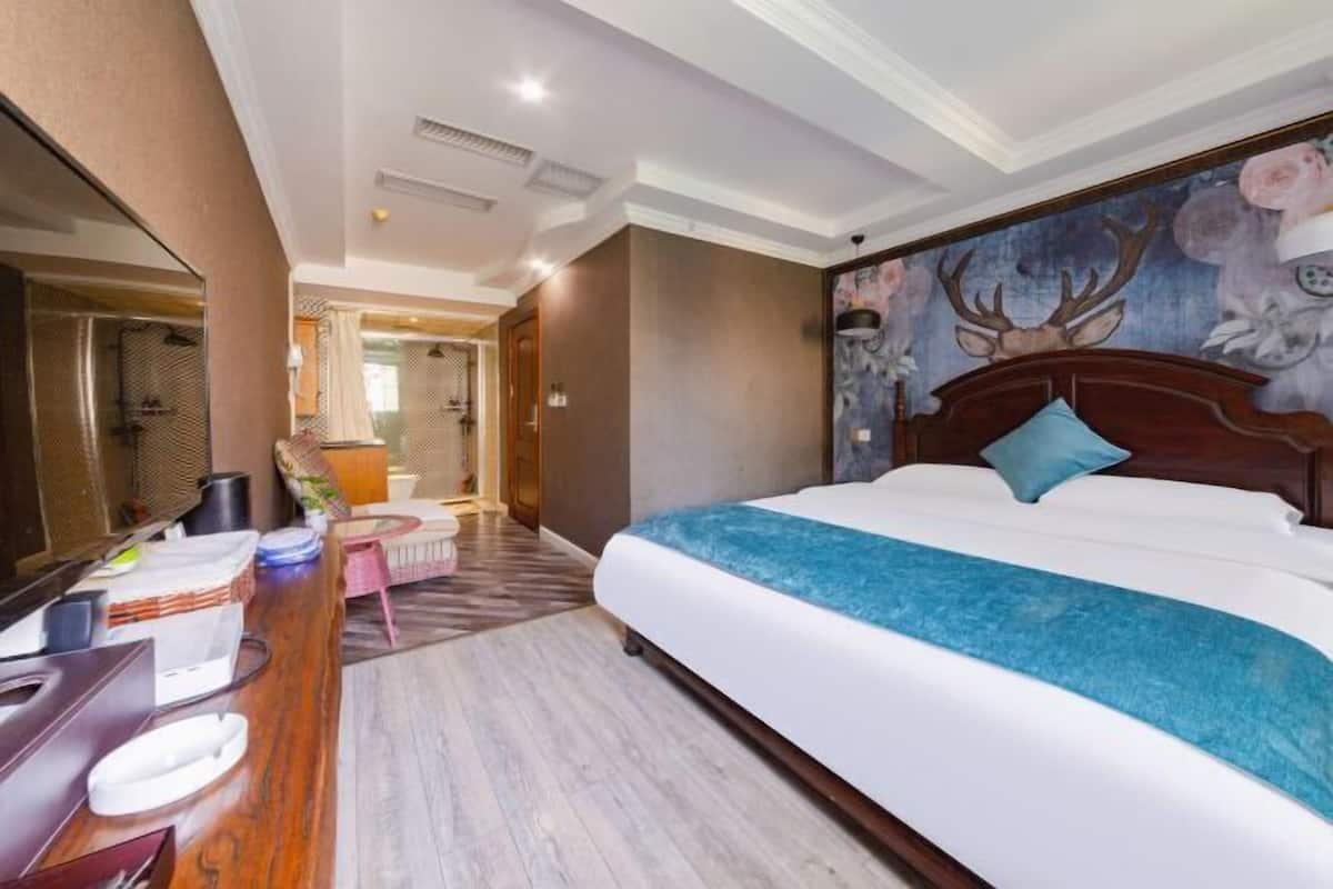 Ein Hotelzimmer mit einem großen Bett, einem Schreibtisch mit Stuhl, einem Spiegel und einem durchgegangene Tür erkennbaren Badezimmer.