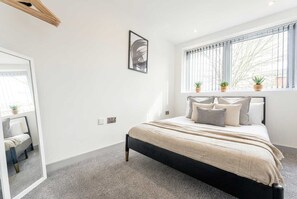 A bedroom with a bed, a window with blinds, a mirror, and a framed picture on the wall. - Chic 1BR Central Apartment Minutes to Station (Wolverhampton)