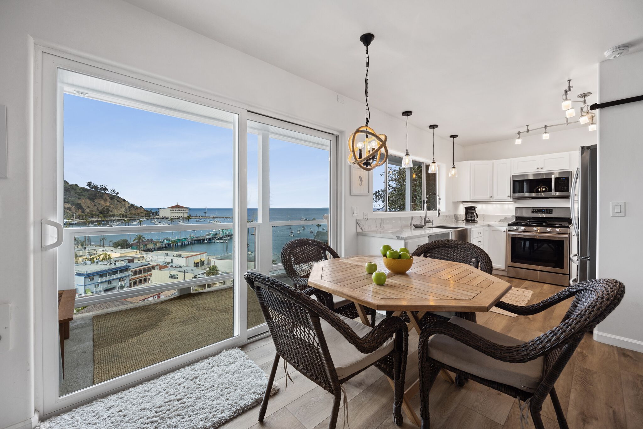 A modern kitchen with a view of the sea, a dining area with wicker chairs, and a large window.