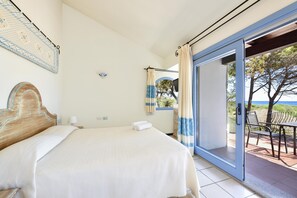A bedroom with a bed, a nightstand, a lamp, a wall-mounted light, and a view of the outdoors through a glass door.