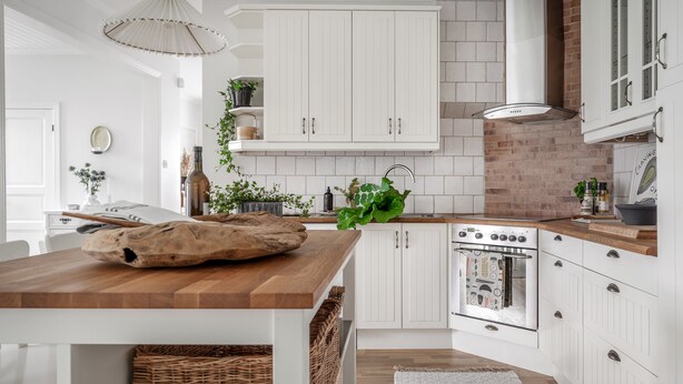 Una cocina moderna con armarios blancos, encimera de madera y pared decorativa de ladrillo.
