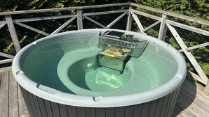 Un jacuzzi en una terraza de madera con barandilla metálica.