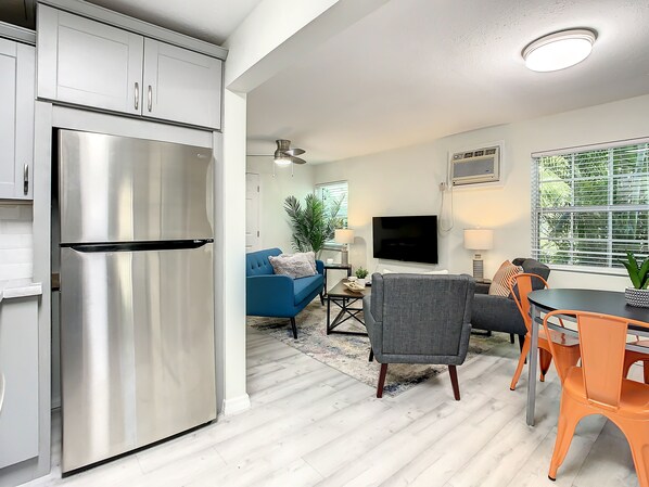 Eine moderne Küche mit einem Edelstahl-Kühlschrank, einem Essbereich mit Tisch und Stühlen, einem blauen Sofa und einem an der Wand montierten Fernseher.