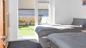 Une chambre avec deux lits, une porte-fenêtre coulissante donnant sur un balcon, et une vue sur un toit recouvert de tuiles et une clôture en bois.