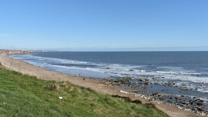 Une plage côtière avec une partie herbeuse en premier plan et une rive rocheuse.
