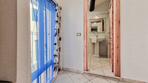 Een hal met een blauw gordijn, een houten deurkozijn en een spiegel die een badkamer met een wastafel weerkaatst.