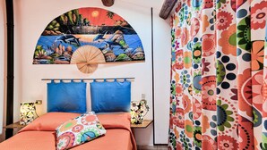 Een slaapkamer met een bed, een wanddecoratie, een ventilator en gordijnen.