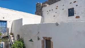 A white building with a blue door, a small window, and a green wall-mounted lamp. - Holiday Home 'Karai Traditional House' with Shared Terrace and Balcony (Astypalea)