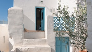 A white building with a blue door and a blue window, a set of stairs leading to a balcony, and a potted olive tree. - Holiday Home 'Karai Traditional House' with Shared Terrace and Balcony (Astypalea)