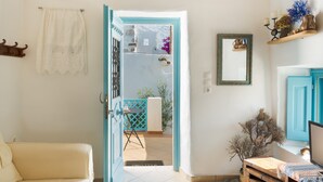 A room with a white sofa, a wooden table, a blue door, and a view of a white building outside. - Holiday Home 'Karai Traditional House' with Shared Terrace and Balcony (Astypalea)