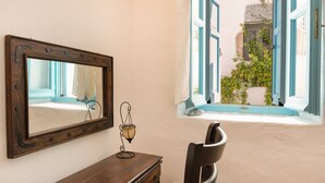 A room with a wooden desk, a chair, a mirror, a window with blue shutters, and a view of a building outside. - Holiday Home 'Karai Traditional House' with Shared Terrace and Balcony (Astypalea)