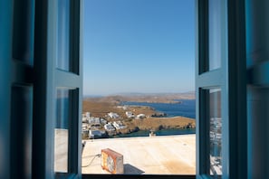 Une vue à travers une fenêtre sur une ville côtière, avec des bâtiments, un ventilateur et un ciel dégagé.