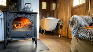 Ein gemütliches Zimmer mit Kaminofen, Badewanne und einem Fellstuhl.