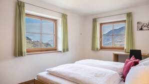 A bedroom with two beds, a desk, and a view of a mountainous landscape through two windows. - Apartment "Gojer Sauvignon" with Mountain View, Garden & Wi-Fi (Cornedo all´Isarco)