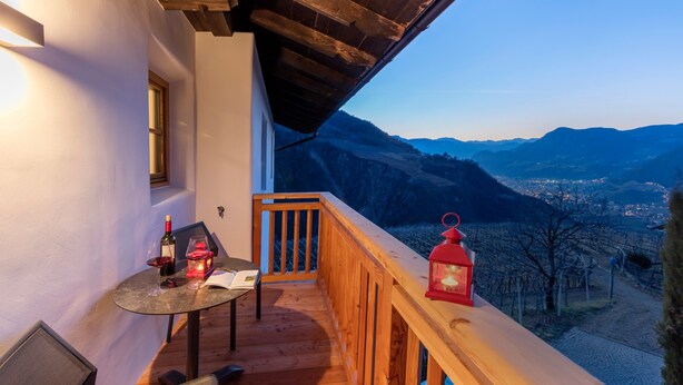 A balcony with a table, chairs, a bottle of wine, and a red lantern. - Apartment "Gojer Sauvignon" with Mountain View, Garden & Wi-Fi (Cornedo all´Isarco)