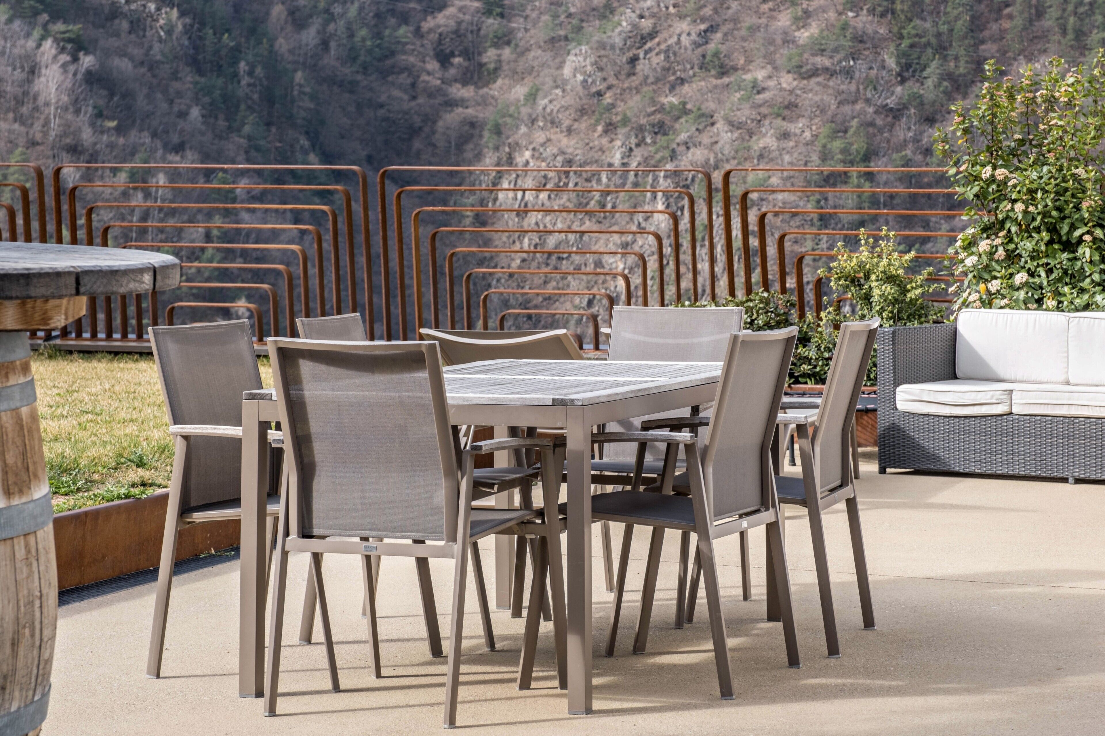 Un patio exterior con una mesa y sillas, un sofá de mimbre y vistas a un paisaje montañoso.