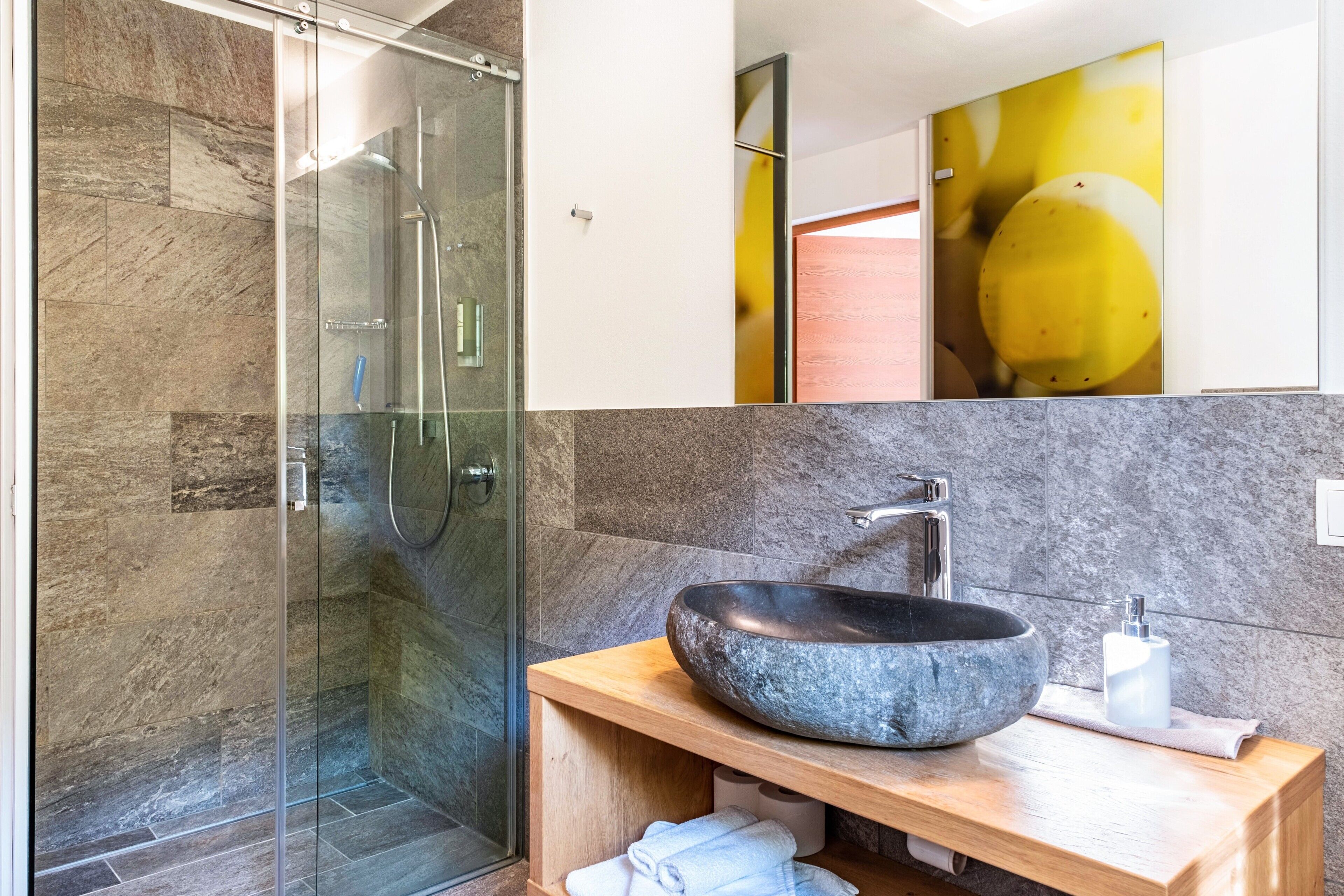 Ein modernes Badezimmer mit einer gläsernen Dusche, einem Steintonne und einem Holzwaschtisch.