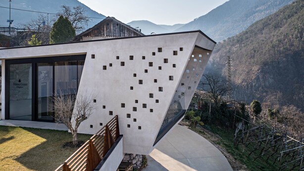 Un edificio moderno con un design angolare distintivo, un ingresso in vetro e una vista sulle montagne sullo sfondo.